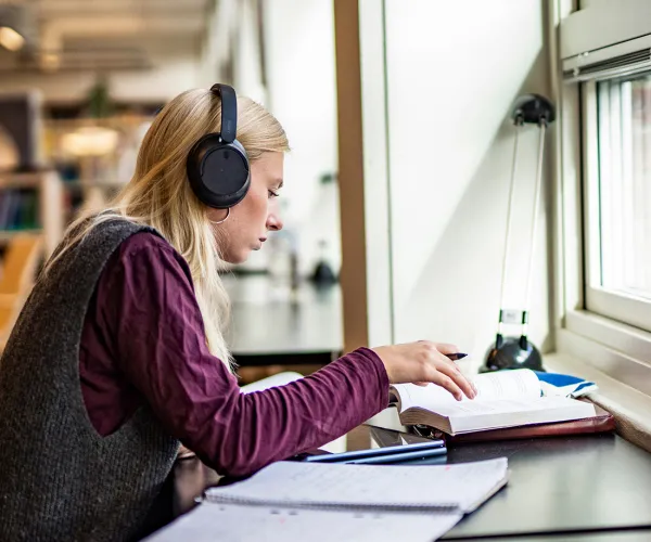 Tjej med lurar och laptop studerar vid skrivbord. Foto.