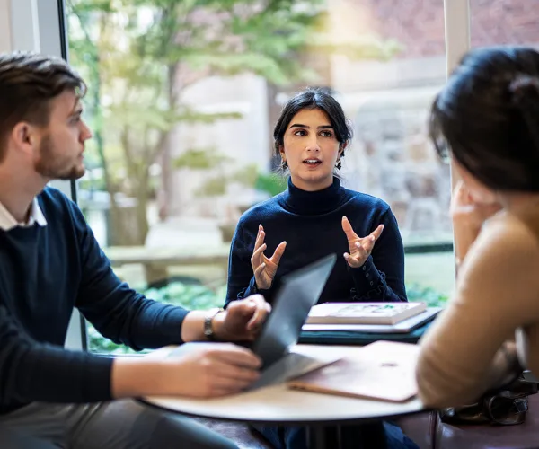 Tre studenter samtalar vid bord. Foto.
