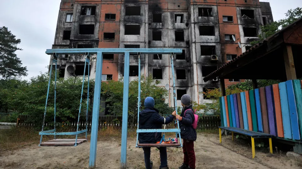  Barn står på en lekplats framför en förstörd byggnad i Kalynivka, norr om Kiev. Foto: Sergei Chuzavkov/AFP.
