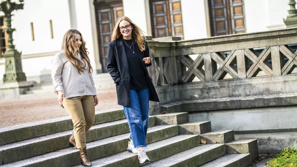 Två kvinnor går nedför en trappa framför Lunds universitets huvudbyggnad.