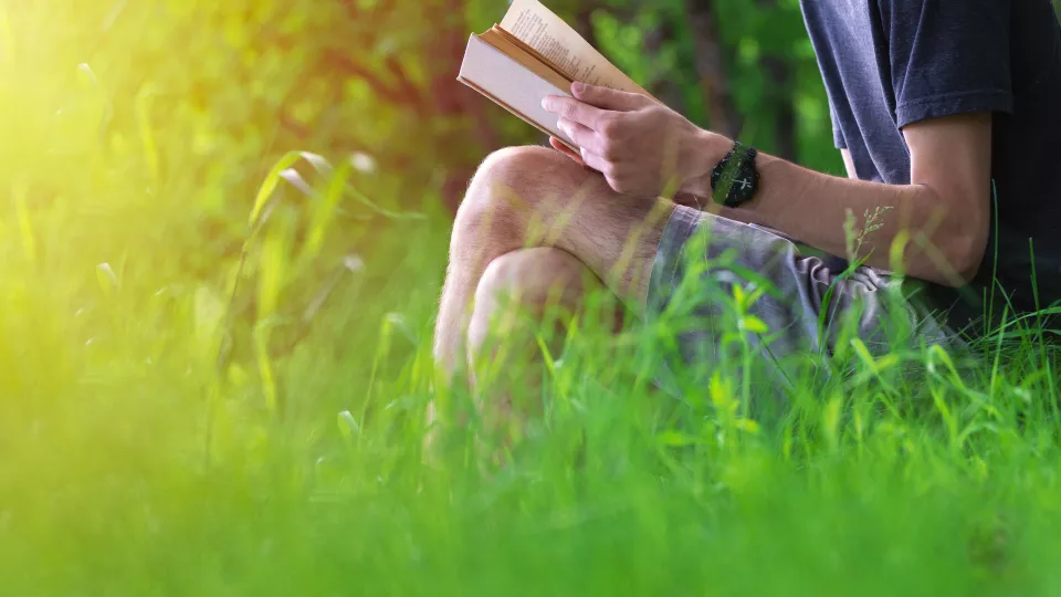 foto på en man som sitter i gröngräset och läser