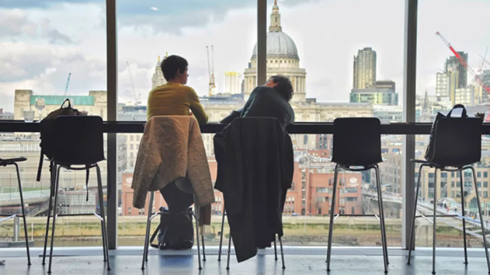 Två personer samtalar vid ett fönster med utsikt över London
