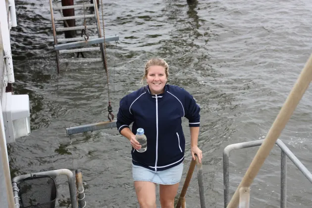 Foto på Isabel Erb som går upp från havet med ett flaska med havsvatten i handen