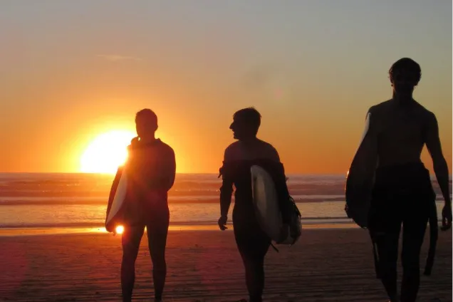 Surfare i kvällsljus på stranden. Foto.