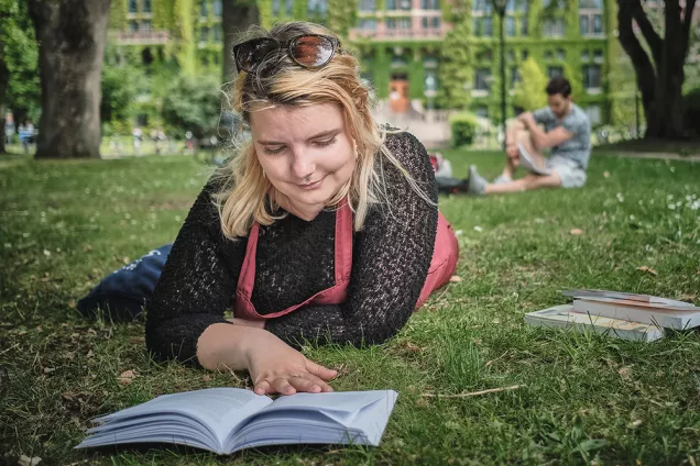 Tjej pluggar i gräset framför Universitetsbiblioteket. Foto.