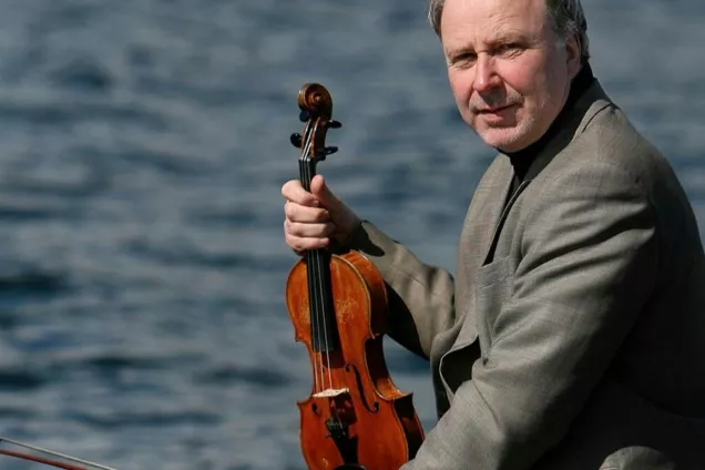 Terje Moe Hansen holsing his violin and looking into the camera. Photo.