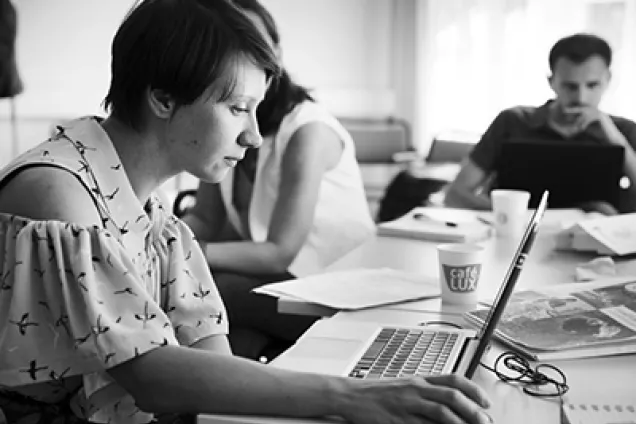 Svartvit bild på personer som sitter runt ett bord med laptops framför sig