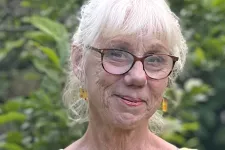Ljushårig kvinna med glasögon framför grönt buskage.