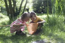 Två barn undersöker vad de fiskat upp ur en damm med sin håv. Foto. 