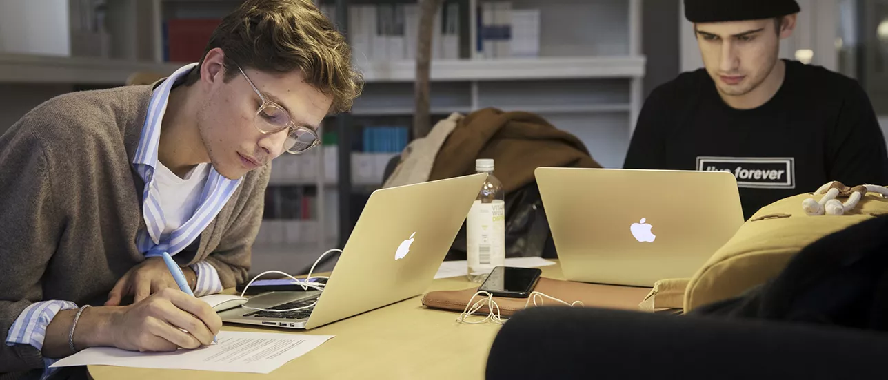 Två studenter sitter vid varsin bärbar dator och pluggar.