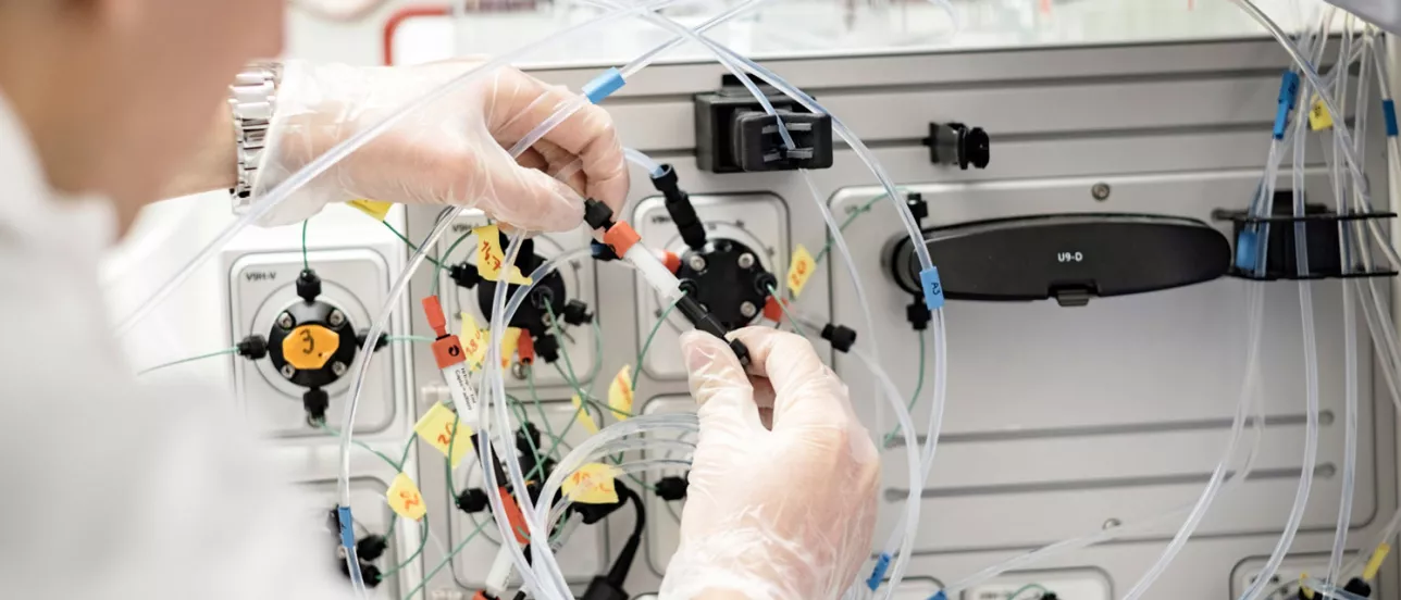 Närbild på händer med plasthandskar som hanterar laboratorieutrustning. Foto.