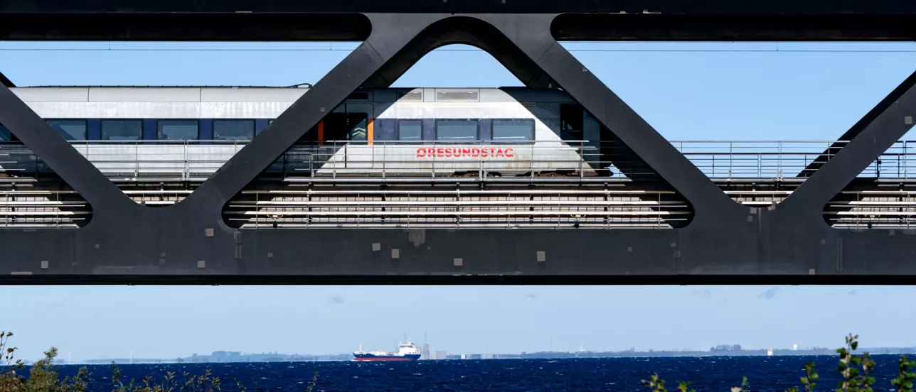 Närbild på Öresundtåg som kör på Öresundsbron, vatten o land i bakgrunden. Foto.