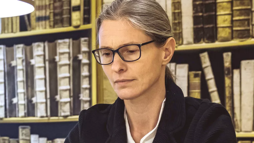 Kvinna med glasögon framför en bokhylla. foto
