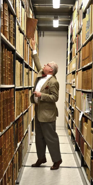 Arkivarie Fredrik Tersmeden sträcker sig efter en bok som står högt uppe på en hylla i ett arkiv.